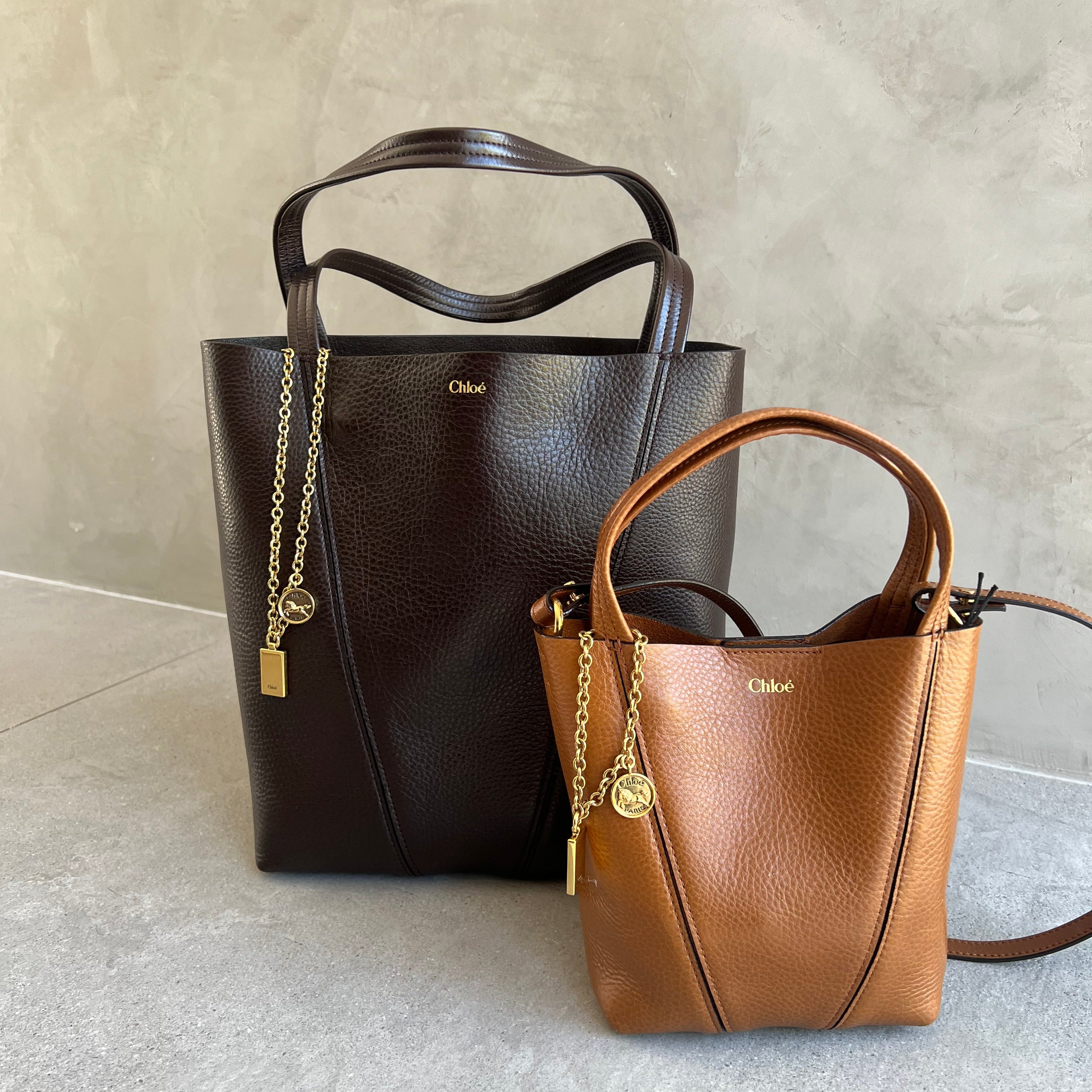 Brown and black handbags with gold accents on a light gray surface