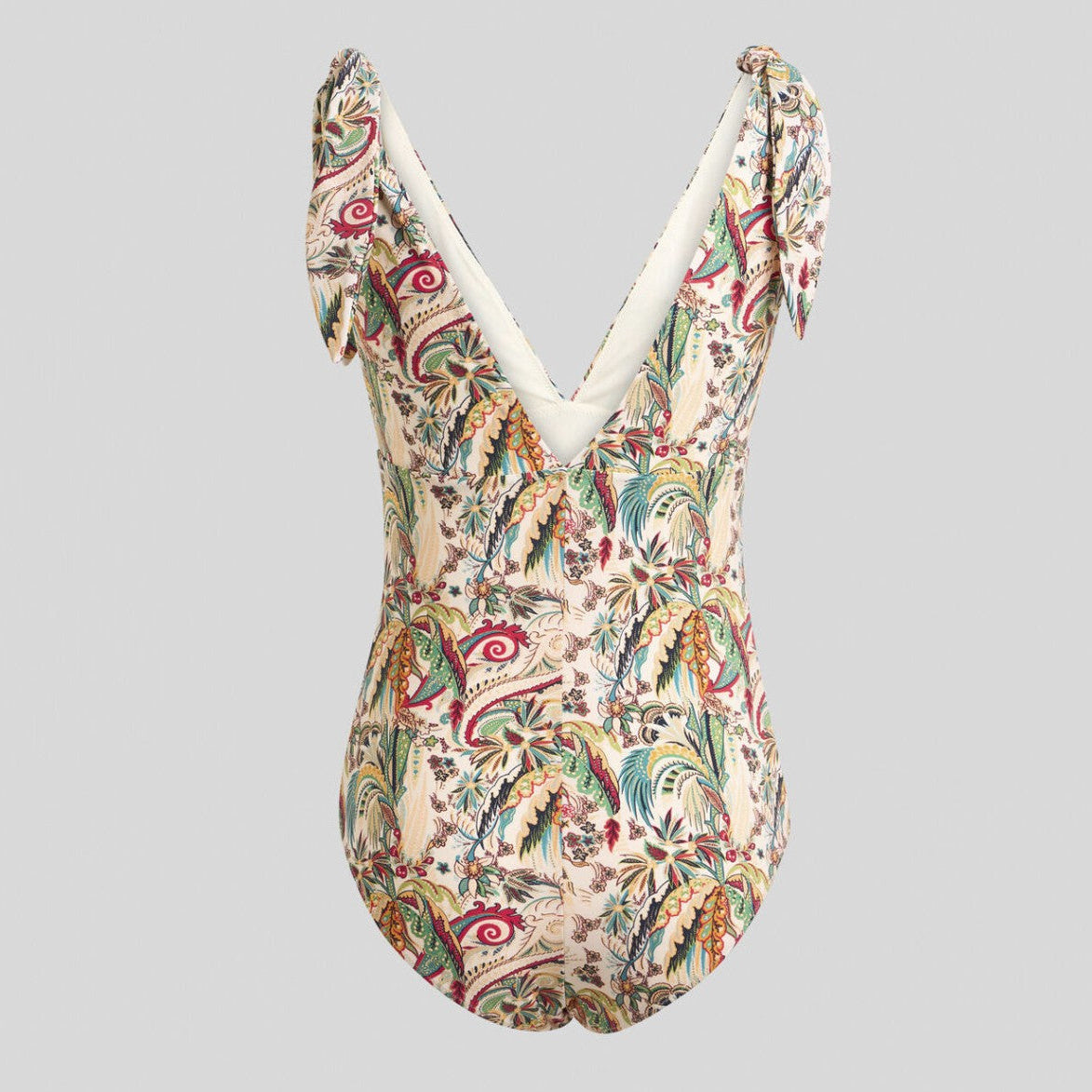 A one-piece swimsuit with a complex multicolor paisley and floral print on a cream base, featuring a deep V-neckline with white trim and tie-shoulder straps, shown against a solid gray background.